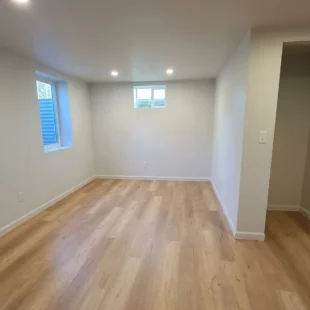 Newly installed light oak luxury vinyl plank flooring in a bright finished basement room with egress windows and white trim, installed by Interstate Flooring on N Halleck St in Portland