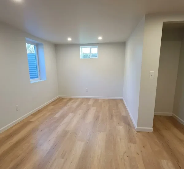 basement-flooring-installation-bedroom-n-halleck-portland Newly installed light oak luxury vinyl plank flooring in a bright finished basement room with egress windows and white trim, installed by Interstate Flooring on N Halleck St in Portland