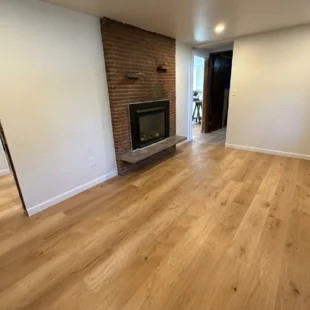 Finished basement living area featuring newly installed light oak luxury vinyl plank flooring laid around a red brick fireplace in a Portland home by Interstate Flooring