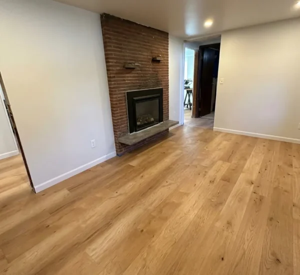 basement-flooring-installation-fireplace-n-halleck-portland Finished basement living area featuring newly installed light oak luxury vinyl plank flooring laid around a red brick fireplace in a Portland home by Interstate Flooring