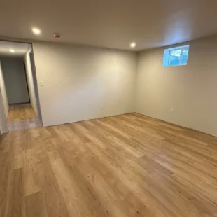 Newly installed light oak luxury vinyl plank flooring extending across a spacious finished basement room and hallway with recessed ceiling lights on N Halleck St in Portland, installed by Interstate Flooring