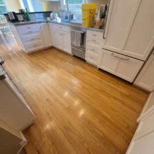 Before photo of a kitchen hardwood floor refinishing project on SW Ridgewood Ave in Portland, OR, showing worn oak flooring with dull, yellowed finish near white cabinetry and stainless steel appliances