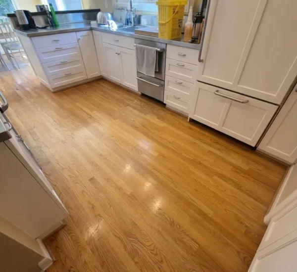 hardwood-floor-refinishing-kitchen-before-sw-ridgewood-ave-portland Before photo of a kitchen hardwood floor refinishing project on SW Ridgewood Ave in Portland, OR, showing worn oak flooring with dull, yellowed finish near white cabinetry and stainless steel appliances