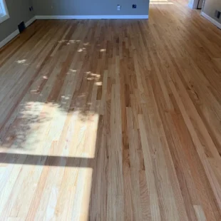 Refinished natural oak hardwood floor in a spacious living room by Interstate Flooring on SW Ridgewood Ave in Portland, showing natural sunlight casting tree shadows across the smooth, clear-coated wood planks