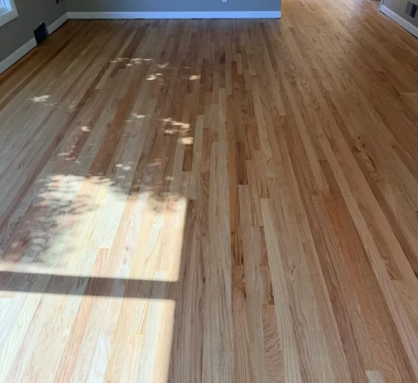 hardwood-floor-refinishing-living-room-sw-ridgewood-ave-portland Refinished natural oak hardwood floor in a spacious living room by Interstate Flooring on SW Ridgewood Ave in Portland, showing natural sunlight casting tree shadows across the smooth, clear-coated wood planks