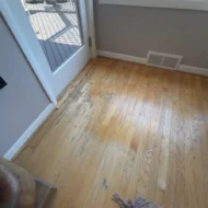 hardwood-floor-refinishing-patio-door-before-sw-ridgewood-ave-portland Before photo of a hardwood floor refinishing project on SW Ridgewood Ave in Portland, OR, showing heavy finish wear, discoloration, and scuffs on oak wood flooring next to a glass patio door