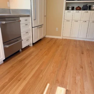 Freshly refinished natural oak hardwood flooring in a modern kitchen by Interstate Flooring on SW Ridgewood Ave in Portland, featuring stainless steel appliances and white cabinetry with custom built-in shelving