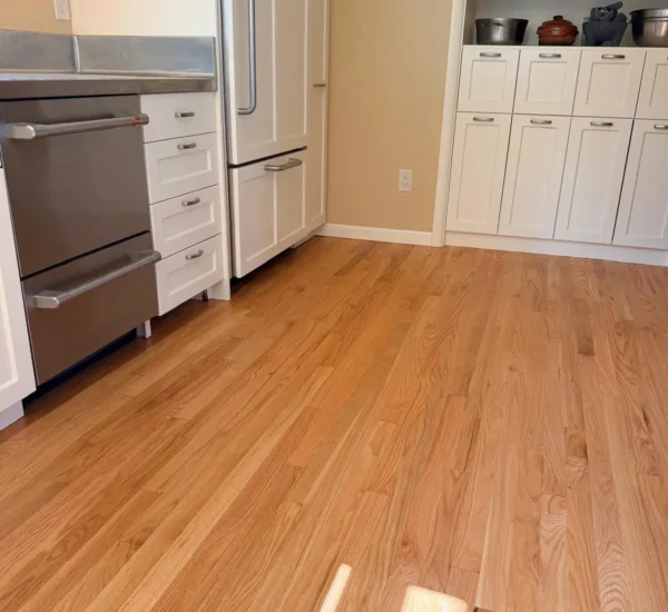 natural-hardwood-floor-refinishing-portland-sw-ridgewood-ave Freshly refinished natural oak hardwood flooring in a modern kitchen by Interstate Flooring on SW Ridgewood Ave in Portland, featuring stainless steel appliances and white cabinetry with custom built-in shelving