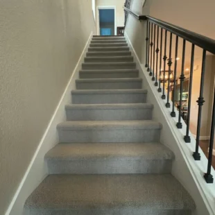 carpet-installation-stairs-portland-or Newly installed plush grey textured carpet on a home staircase with white risers and wrought iron railing in Portland, Oregon.