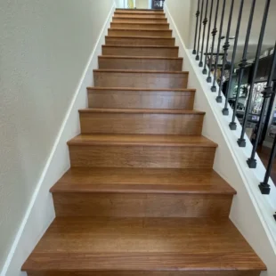 hardwood-staircase-remodel-iron-railing-portland-or Full straight view looking up a newly installed hardwood staircase with matching wood risers, white trim, and black wrought iron railing balusters in Portland, Oregon