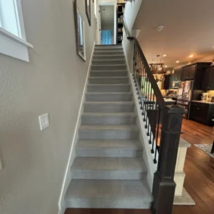 stair-carpet-installation-portland-or Wide view of a completed staircase carpet installation featuring light grey patterned carpeting alongside dark wood railing and open kitchen flooring in Portland, Oregon